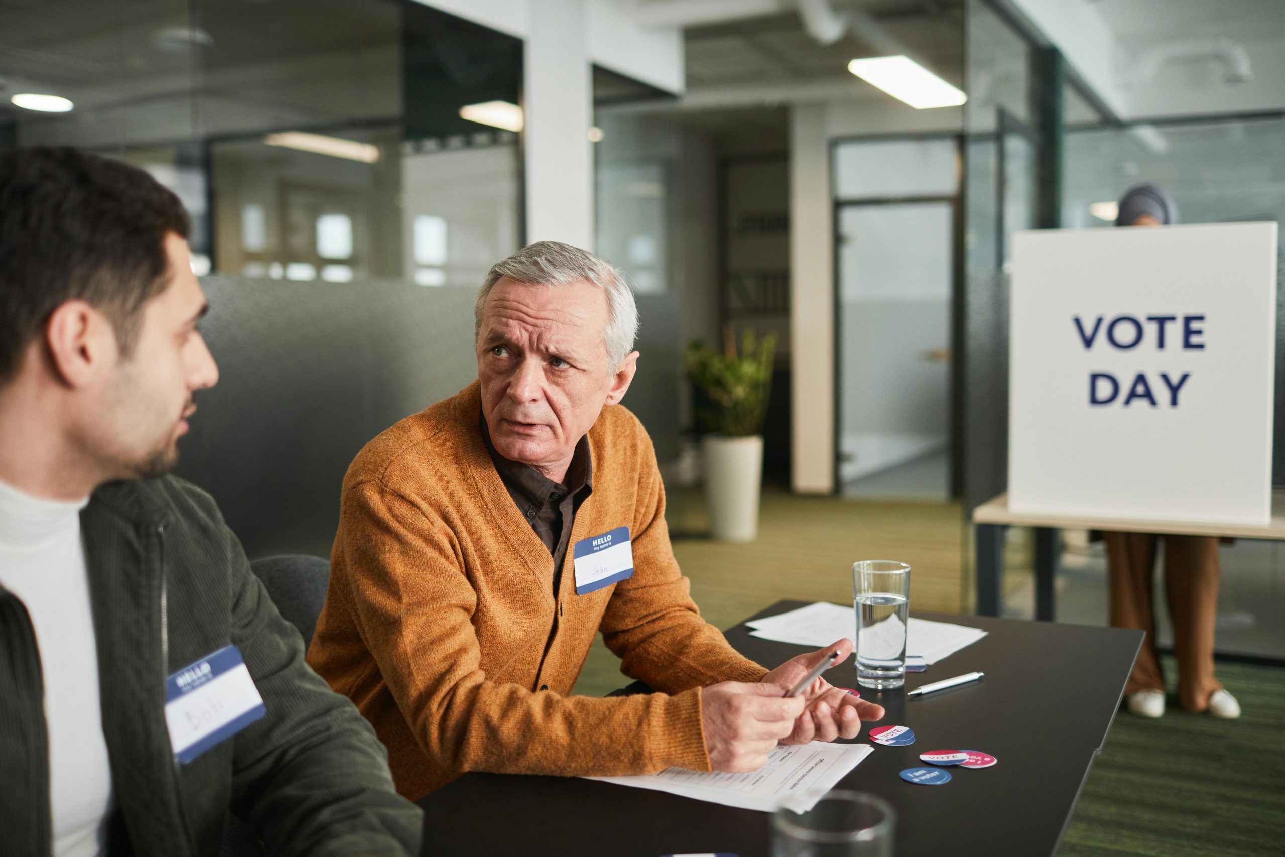 Two election officials discuss voting day logistics inside a modern office environment.